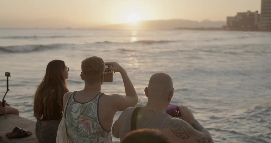 People take photos on a beach at sunset