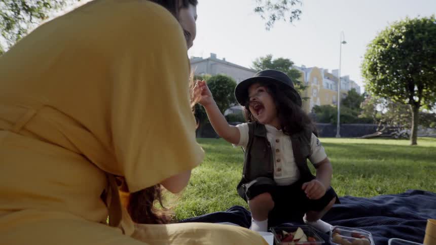 A playful young child high fiving mother while sitting on picnic blanket.