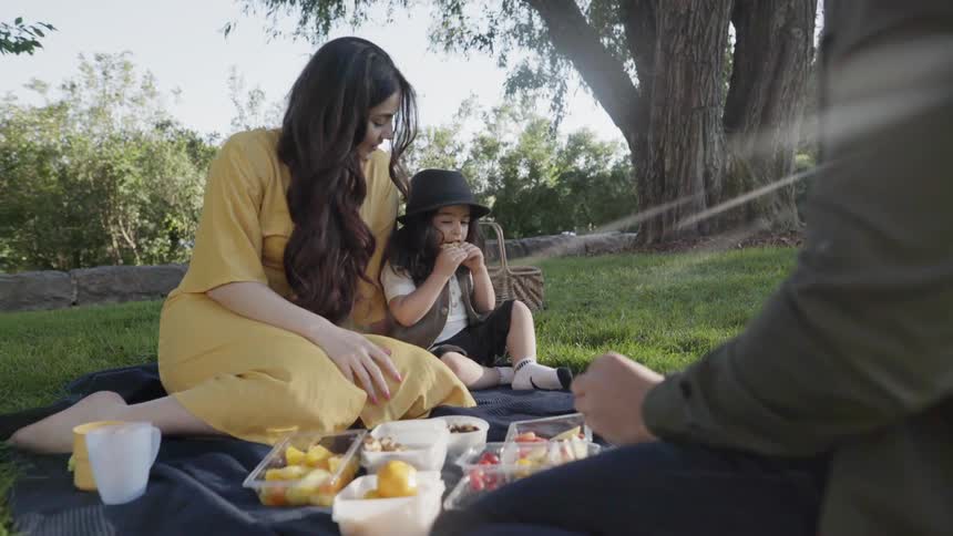 A young mother and child eating fruits while picnicking in the park.