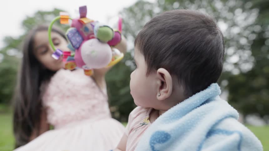 A girl and baby play on a blanket on a lawn