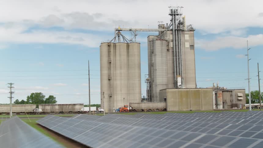 Solar panels cover the ground in front of silos
