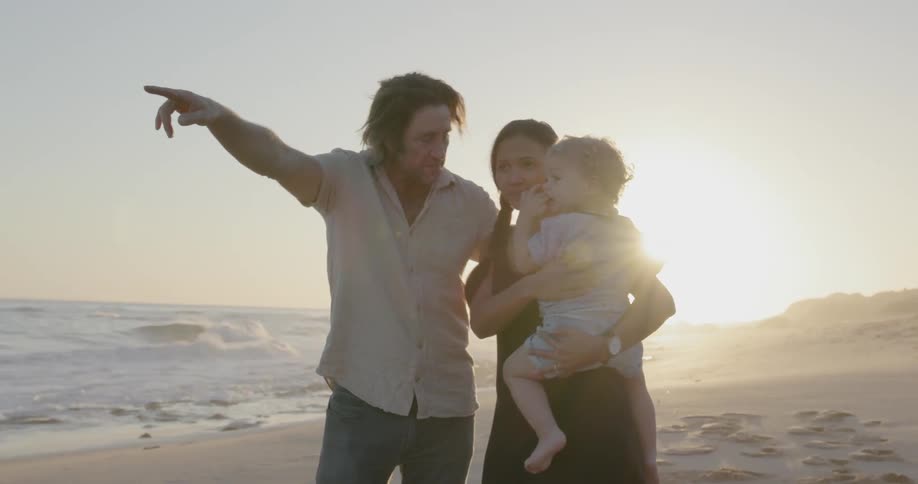 Man woman and child stand on the beach and the man smiles and points