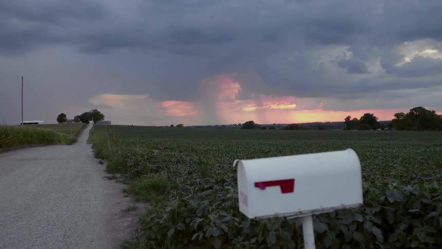 Rain falls from clouds over a rural area at sunset
