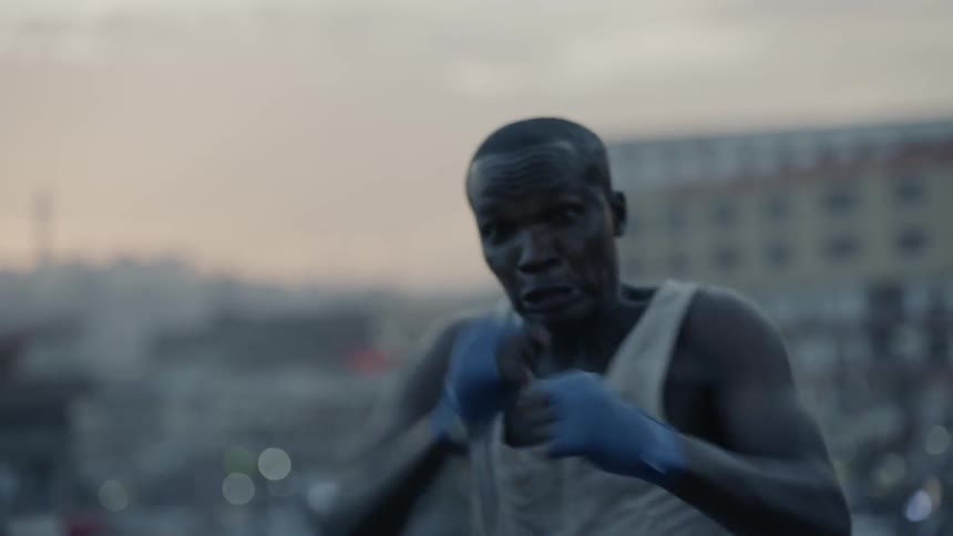 A boxer punches the air in a city at sunset