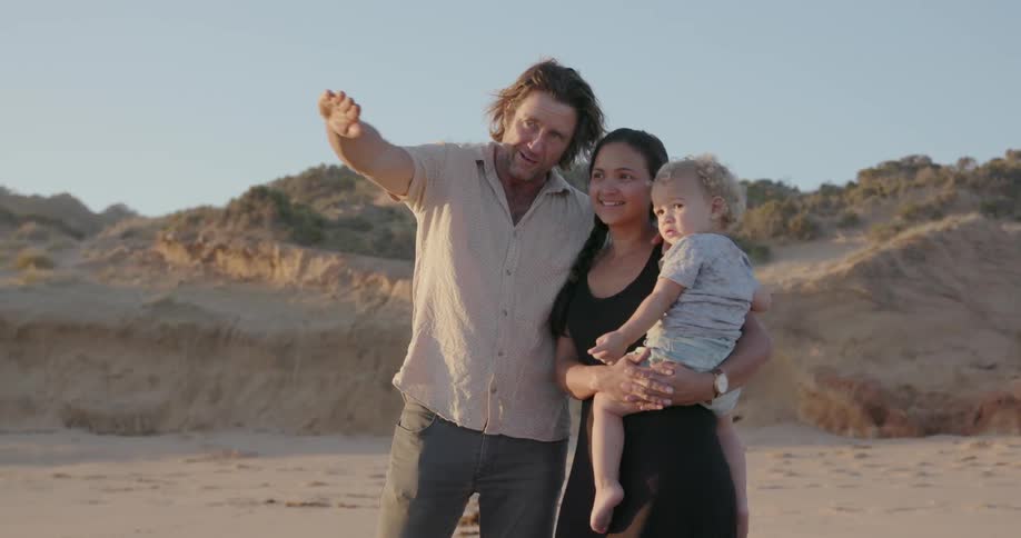 A young family stands on a beach