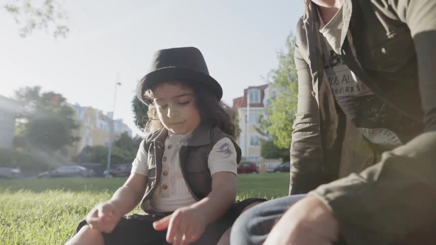 A young child sitting on green grass playing next to father outdoors.