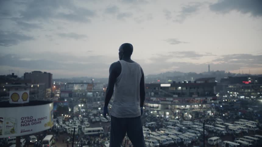 A man is standing on a rooftop looking out at a city at dusk