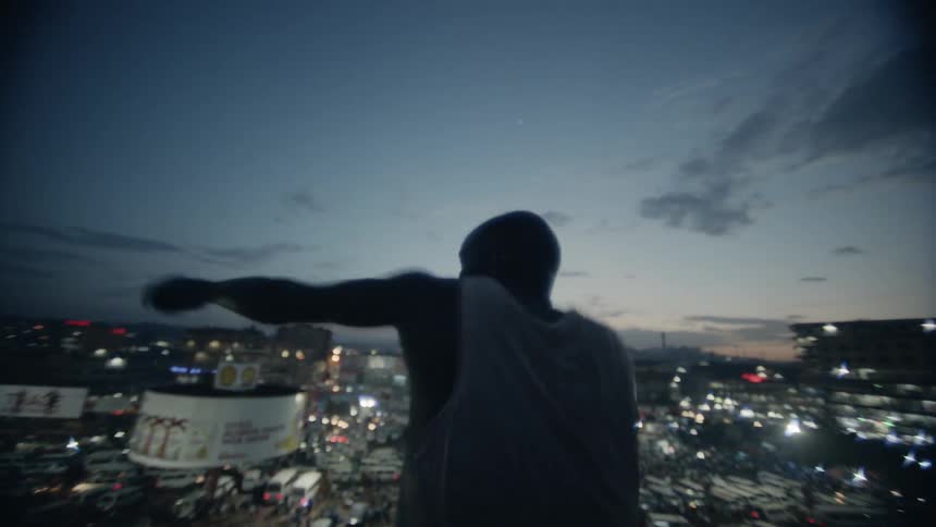 A boxer punches the air on a building rooftop at dusk