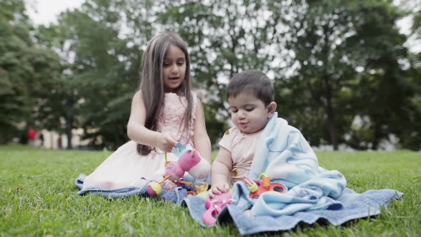 A young girl and baby play on a grassy lawn