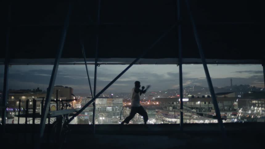 A boxer is shadow boxing on a rooftop at night