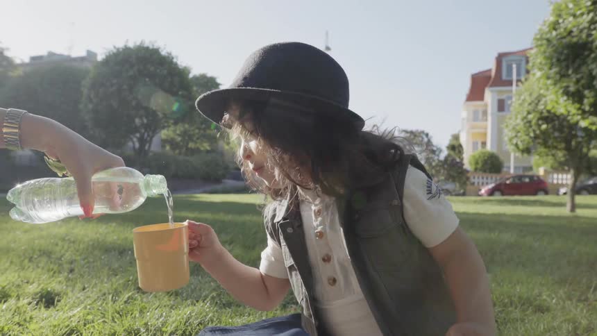 A parent pouring fresh water into a yellow cup held by young child.