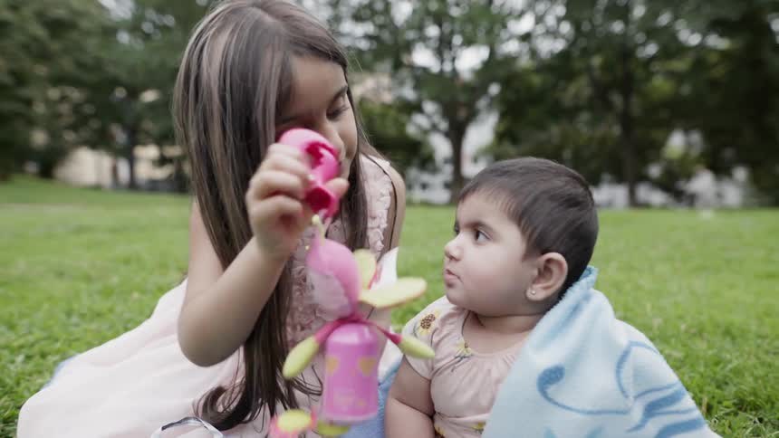 Child waves a toy in front of a baby while sitting outside on the lawn