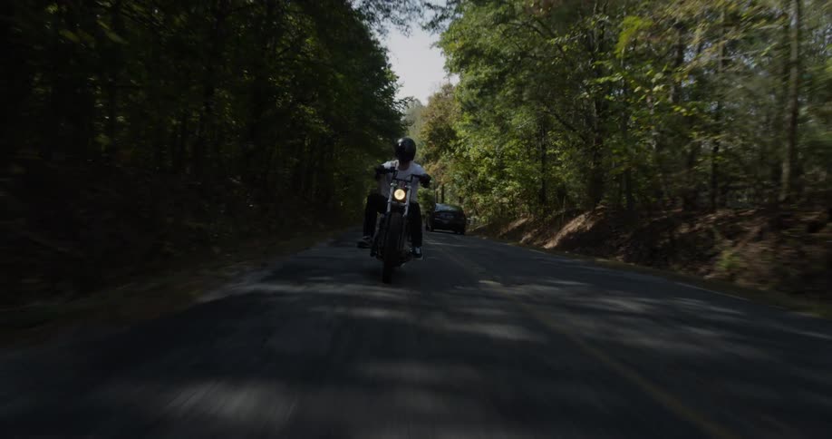 A man is riding a motorcycle on a road through a forest on a sunny day