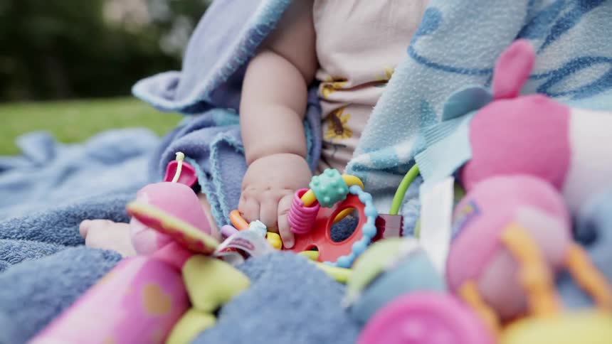 Child plays with toys sitting on a blanket outside