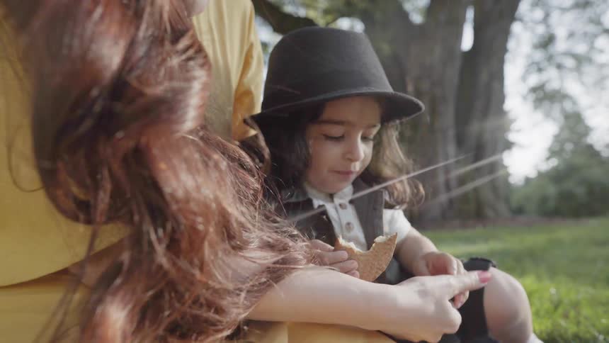A mother feeding a piece of bread to her young child outdoors.