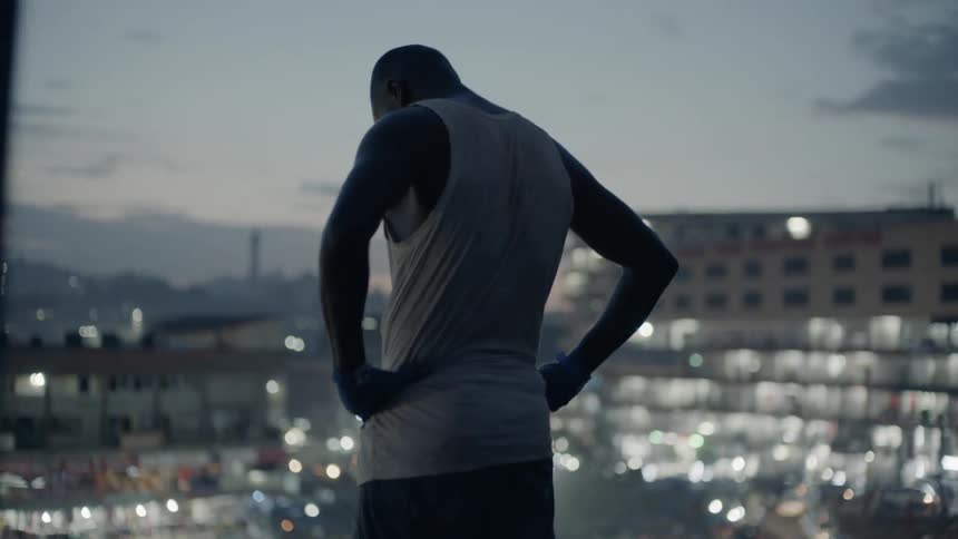 Man stands looking at a city lit up below in the evening