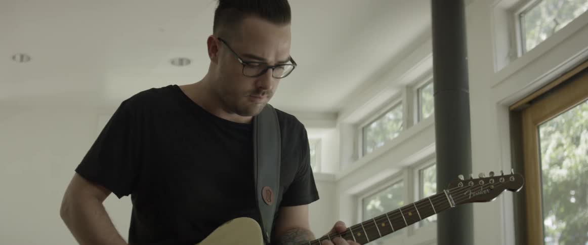 Man is standing and playing guitar inside house