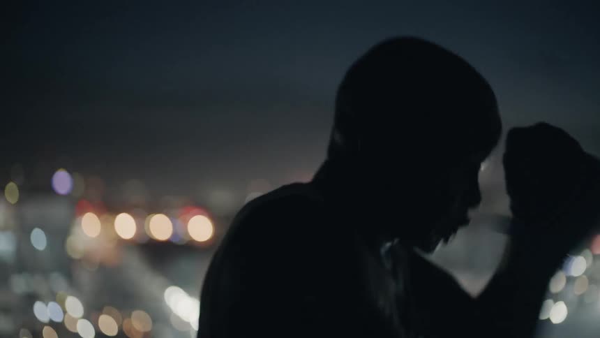 A boxer punches the air in a city at night
