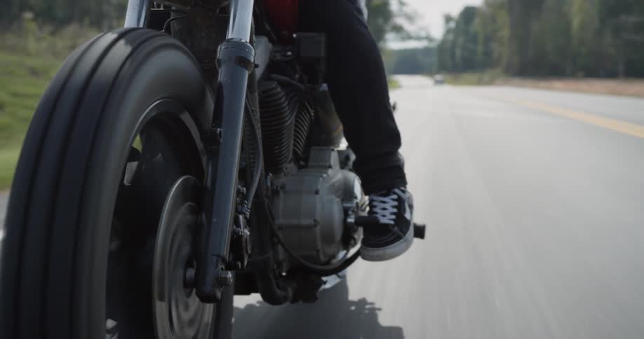 Person drives a motorcycle on a tree lined country road
