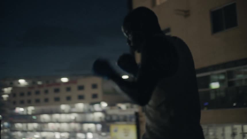 A boxer punches the air in a city at night