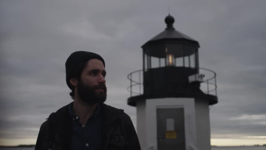 A man walks away from a lighthouse on a cloudy day