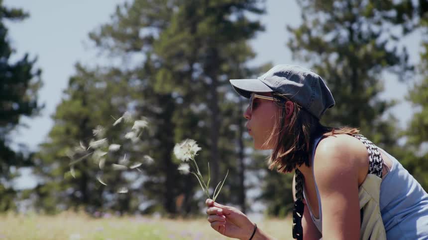 Woman stands in a field and blows a dandelion puff