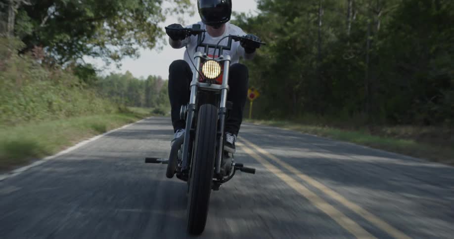 Man rides a motorcycle down the highway near the trees