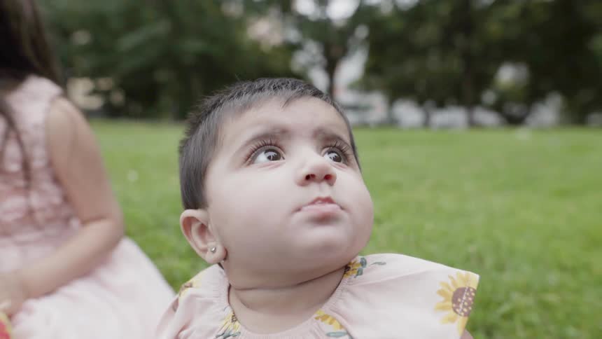 Young girl and baby sit on grass in park