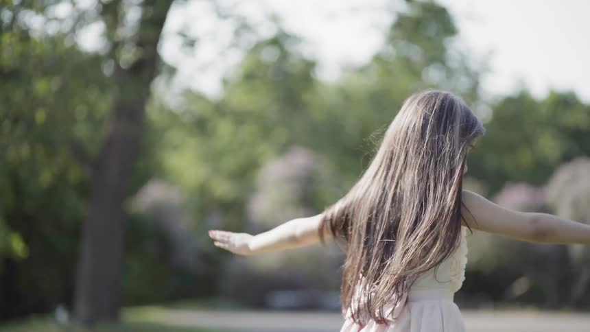 A little girl is dancing and twirling outside in daylight