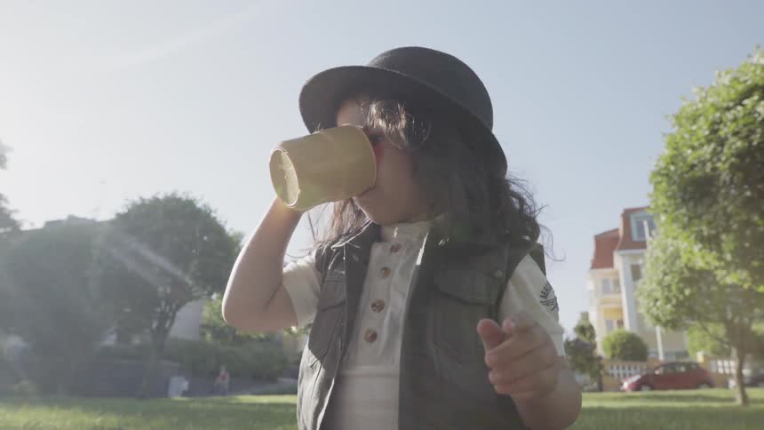 A child wearing a black hat drinking water from a yellow cup outdoors.
