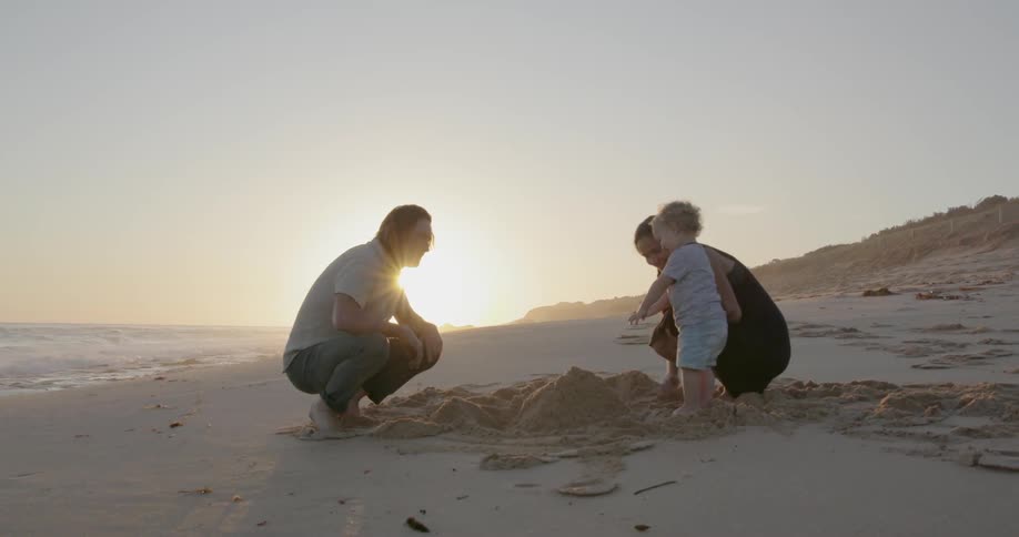 A young family builds a sandcastle on a beach at sunset