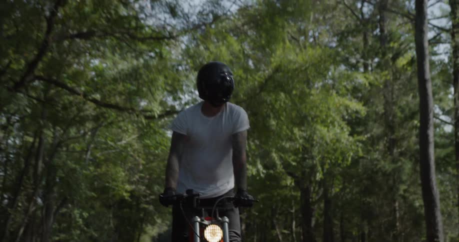 Man is standing up while riding motorcycle on forest highway