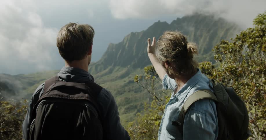 Two men wearing backpacks are talking and observing mountain wilderness