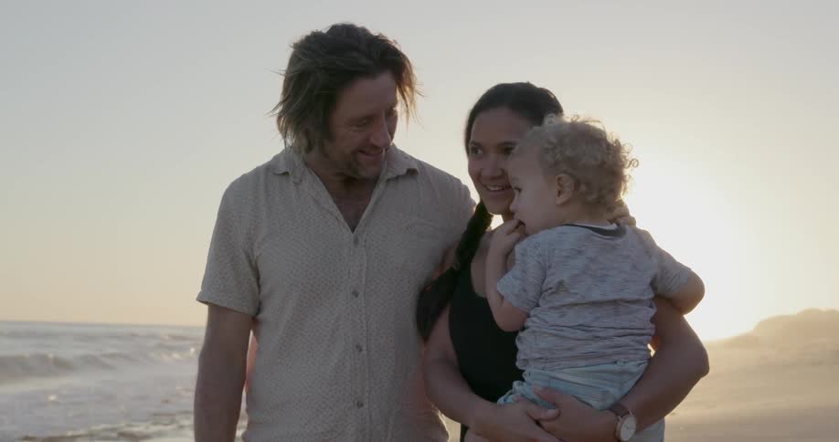 A young family stands on a beach at sunset