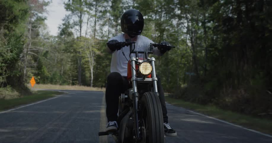 Man rides a motorcycle down the road near the trees