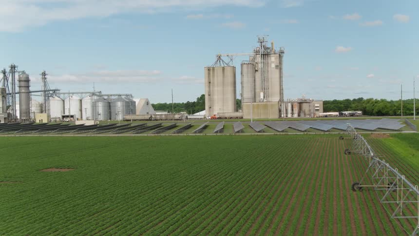 Solar panels sit in a farm field near silos