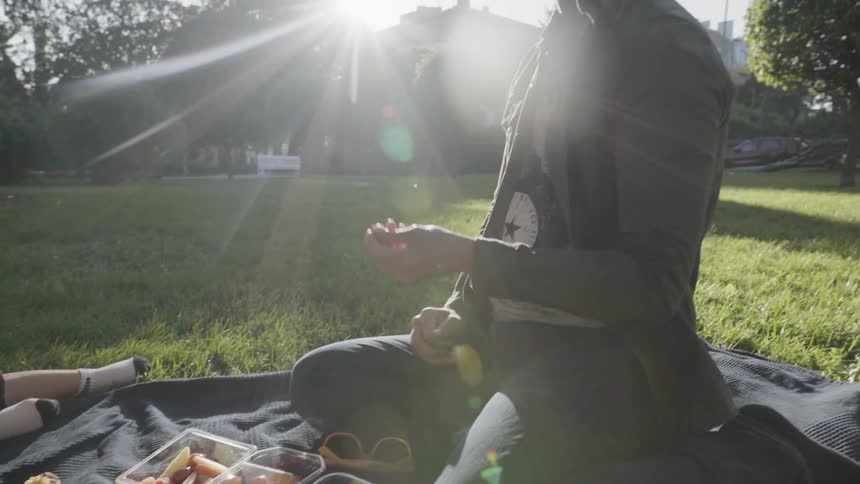 A man eating fresh grapes while sitting on picnic blanket in park.