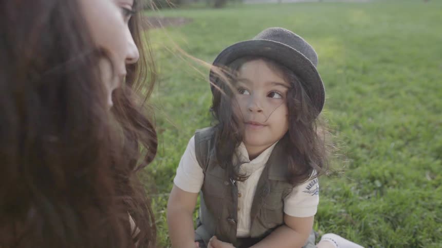 A young boy wearing a hat looks up happily at his mother outdoors.