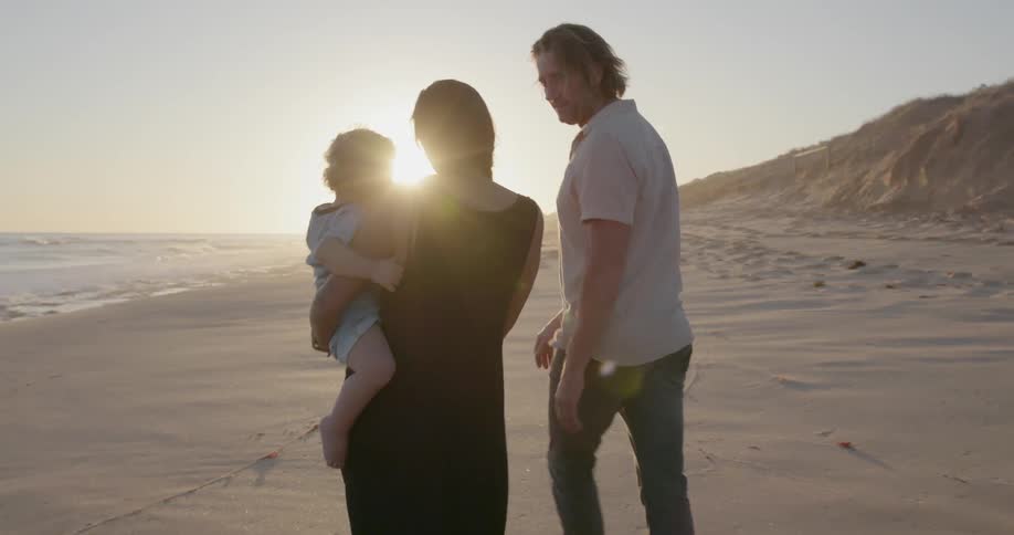A young family walks on a beach at sunset