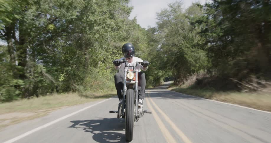 Man is riding motorcycle on sunny highway surrounded by trees