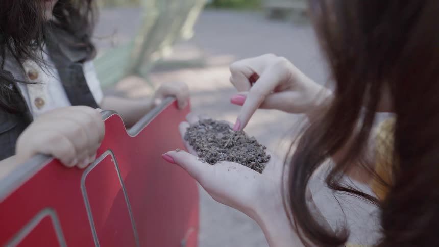 A woman holding soil and seeds in hands with a child outdoors at park.