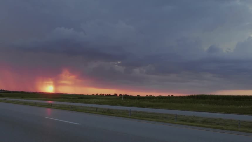 Sun shines through clouds pouring rain on flat land