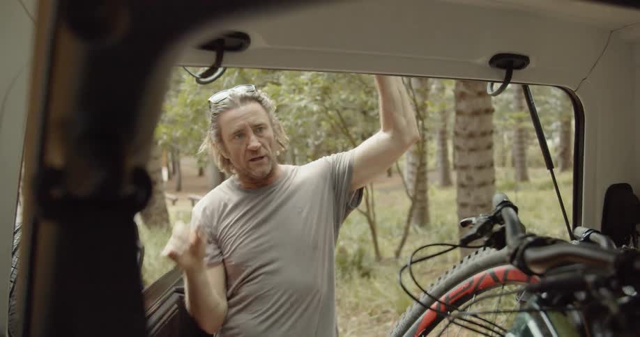 A man is getting a mountain bike out of an suv in daylight
