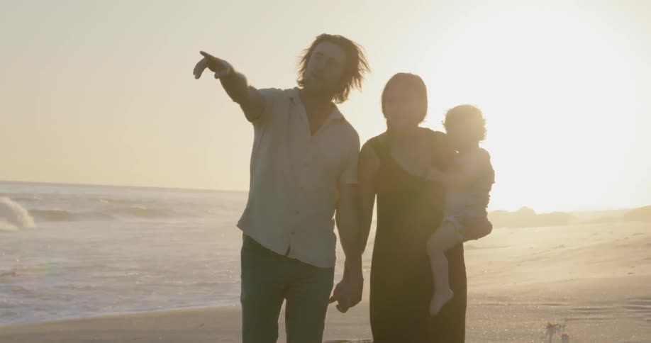 A young family walks on a beach at sunset