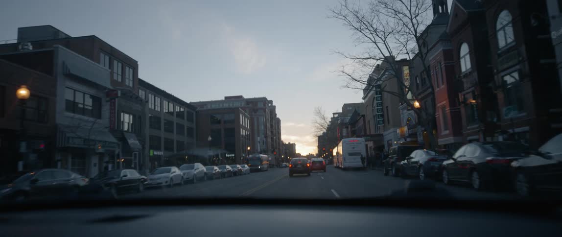 A car travels on a city road at dusk