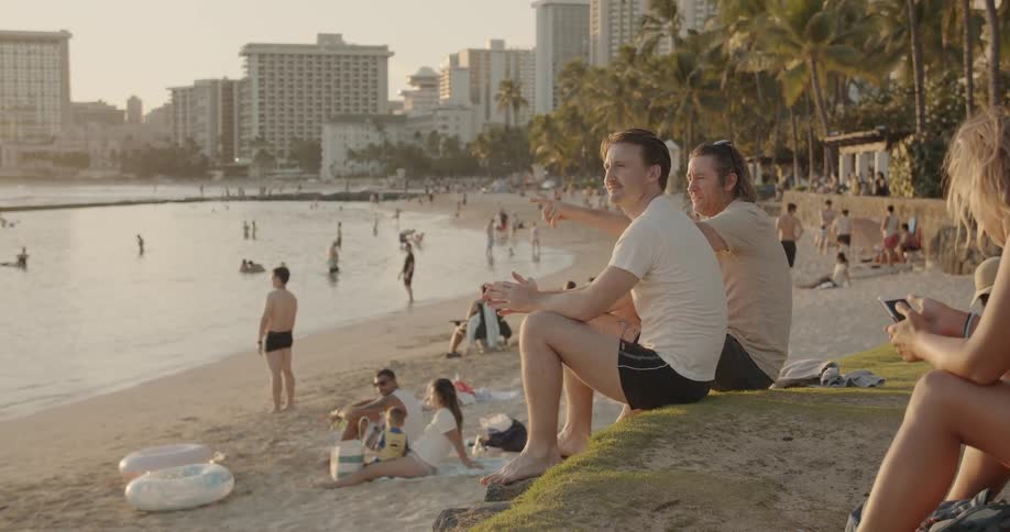 Two men sit side by side on a small hill on the beach