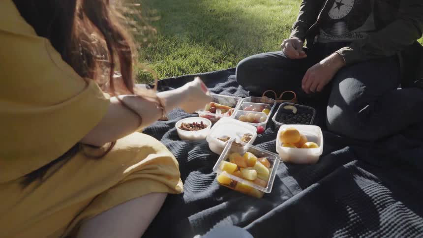 A family sitting together on a dark blanket enjoying a outdoor picnic.