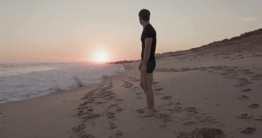 Man stretches on a beach at sunset