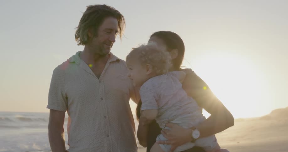 A young family stands on a beach at sunset