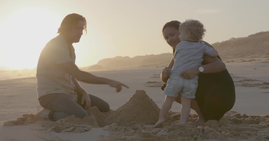 A young family builds a sand castle on a beach at sunset
